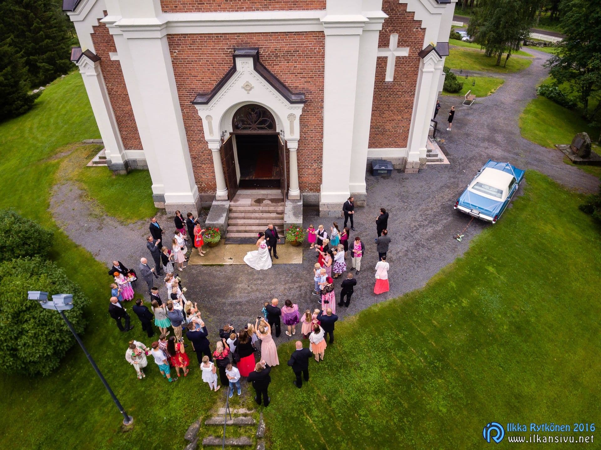 A wedding couple and guests outside the church steps seen from above