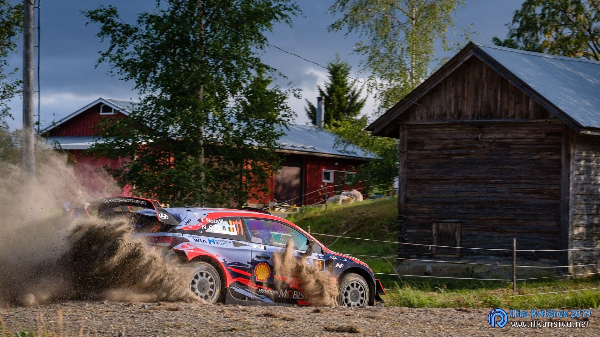 Thierry Neuville ja Nicolas Gilsoul, Hyundai i20 Coupe WRC numero 11, soraa lennättävässä mutkassa puurakennusten edustalla – Neste Rally Finland 2019