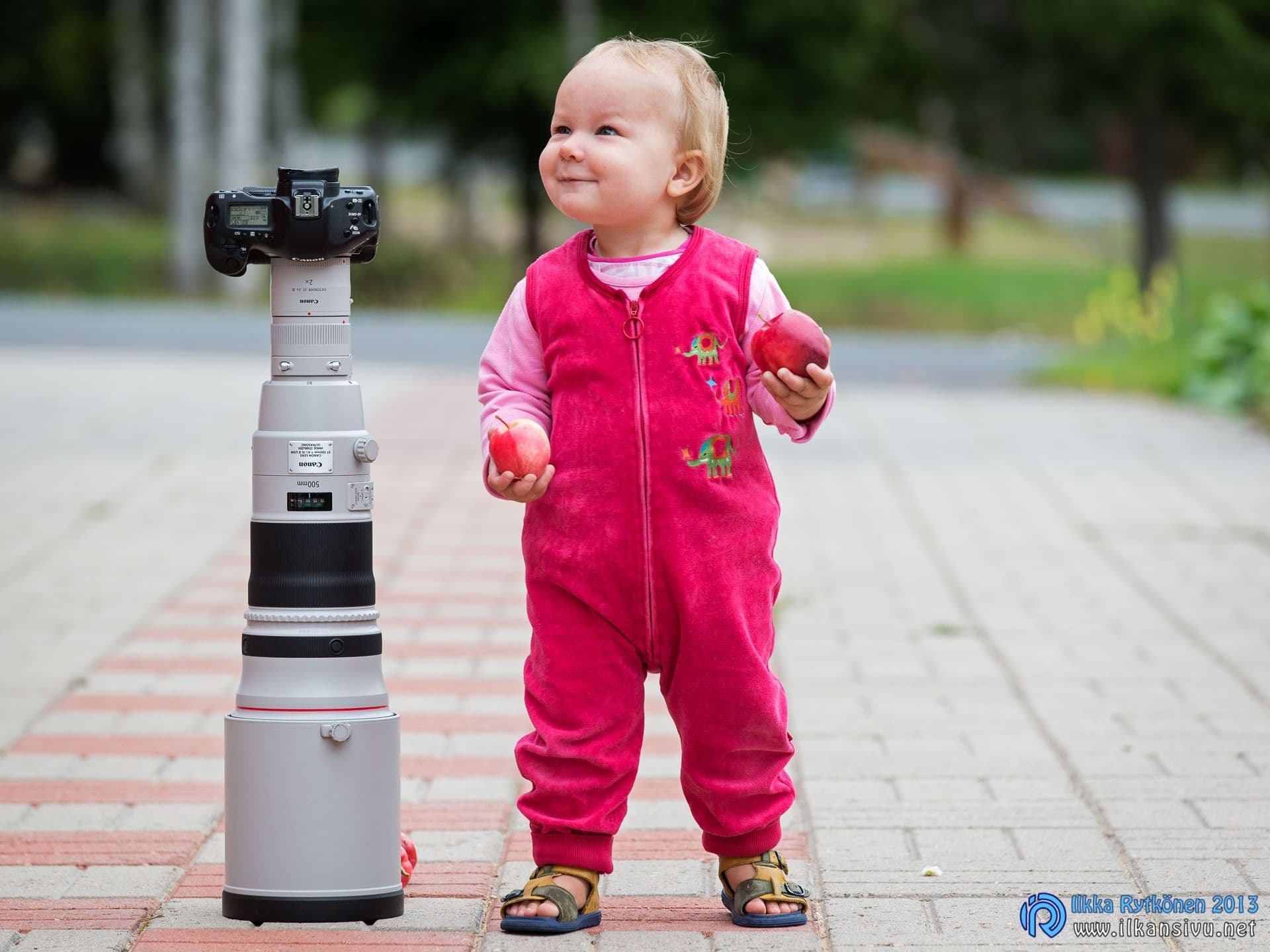 A small child stands beside a large telephoto lens and camera