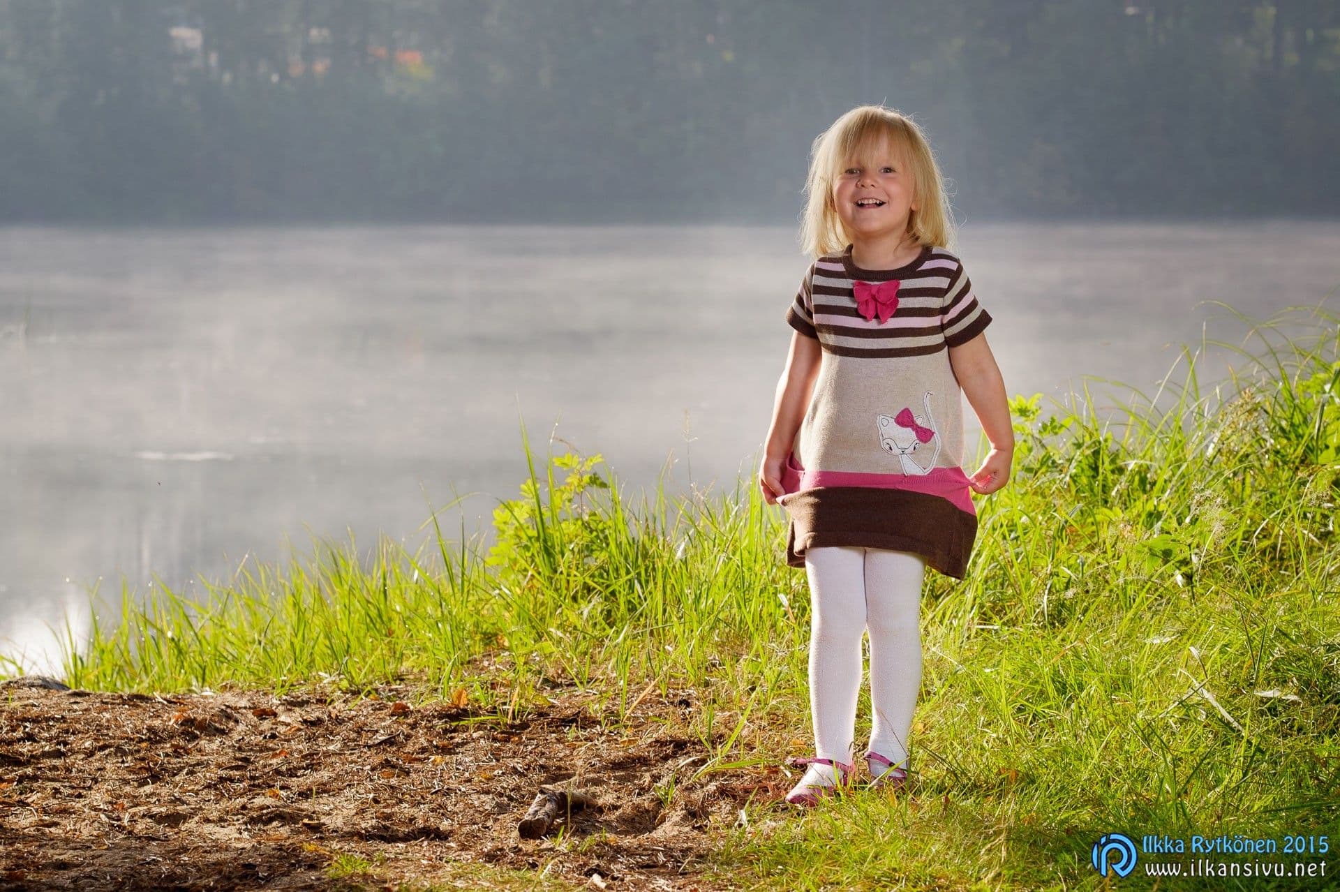 A child stands on grass beside misty water