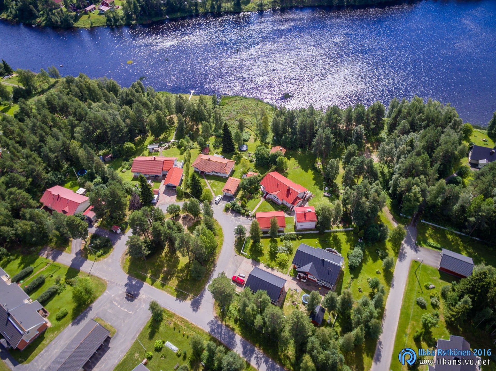 Aerial view of red-roofed buildings among trees beside the water